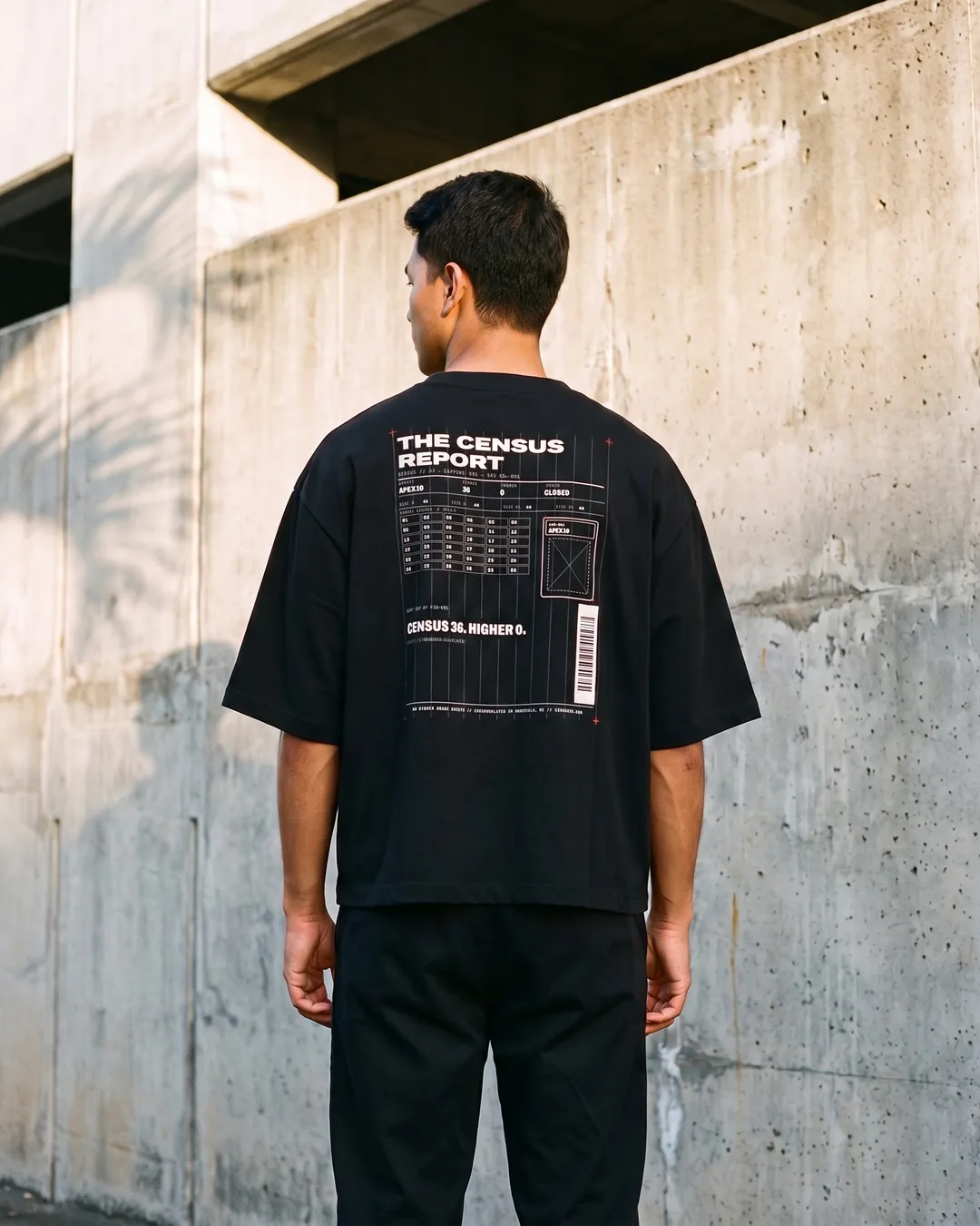 C36-001 vault tee in black, worn from the back: The Census Report ledger print against a raw concrete wall in Kakaʻako, Honolulu